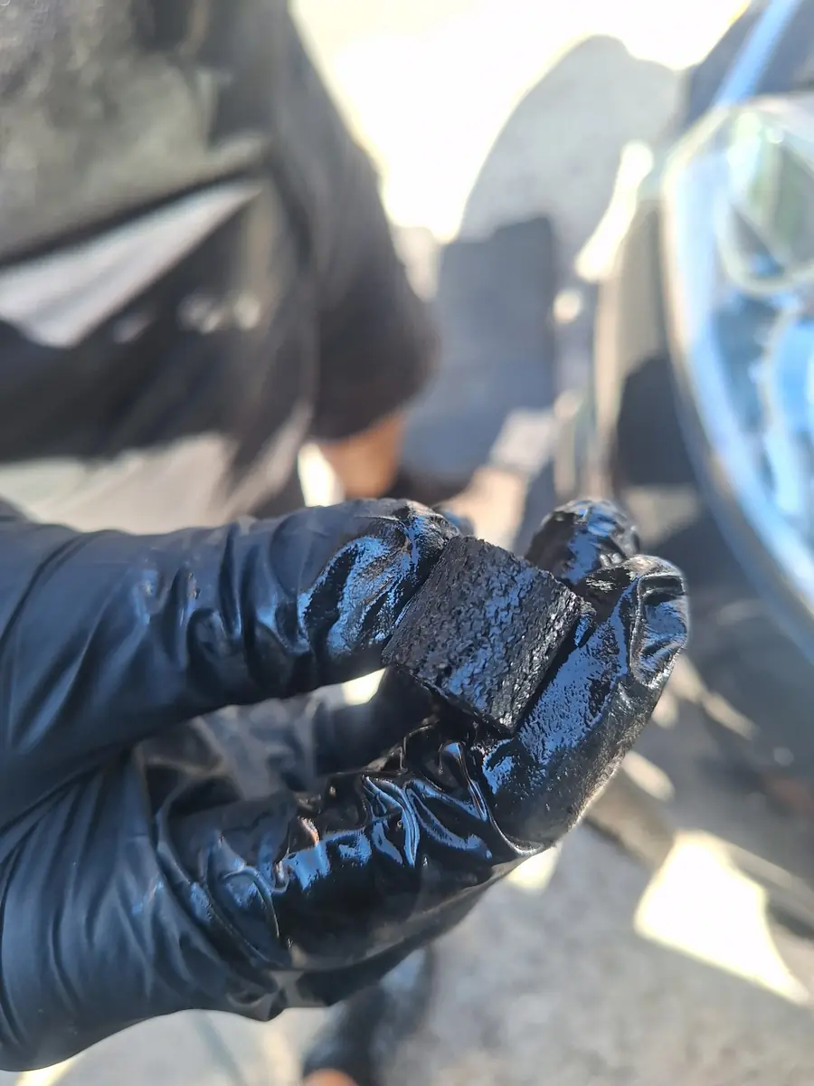 A piece of old belt material held in an oily gloved hand