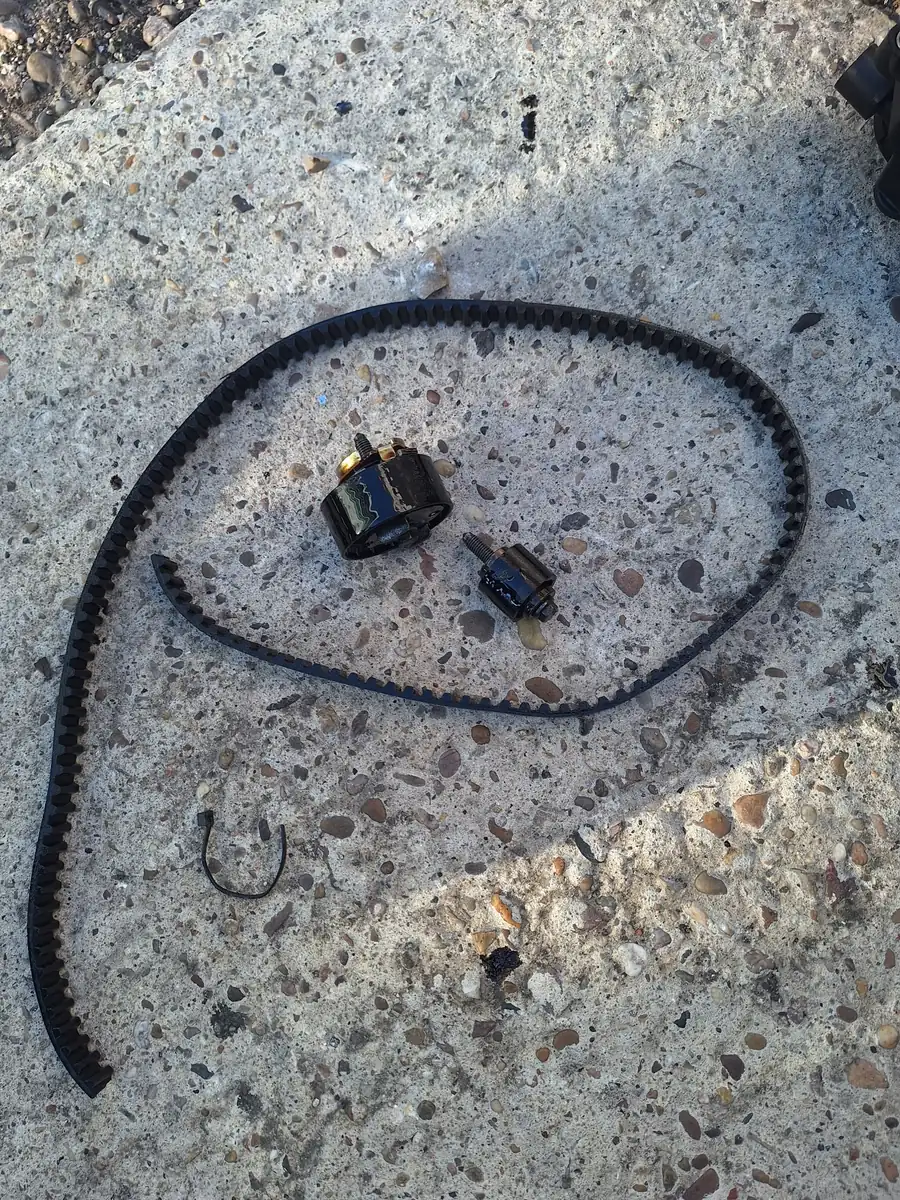 An old belt and oil covered tensioners laid out on the ground after removal
