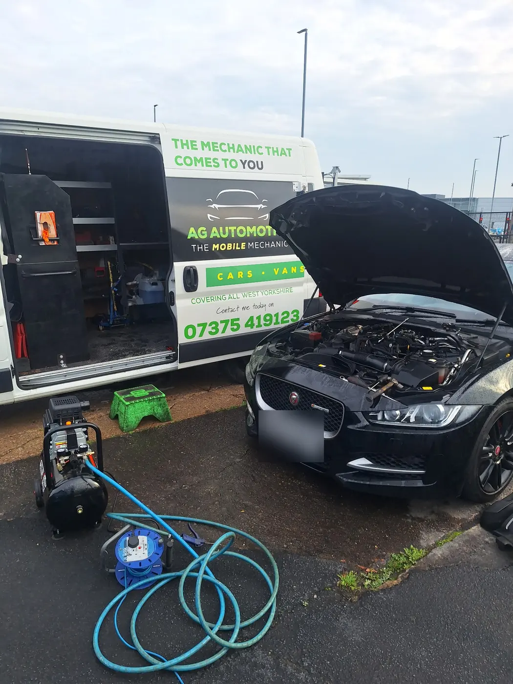 The AG Automotive van with its side door open showing shelves of tools, next to a black car with its bonnet up and an air compressor on the ground